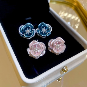 Detailed macro view of pink and blue rose stud earrings with pearls in a black velvet box
