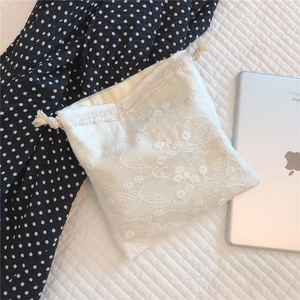 Detail of floral lace embroidery and beige drawstring closure on a cotton pouch