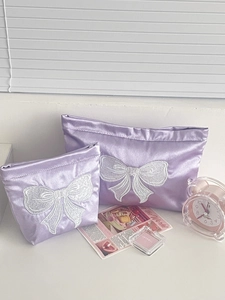 Detailed view of two purple satin makeup bags with elegant white bow embroidery