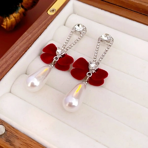 Detailed shot of red velvet bow earrings with teardrop pearls and crystals in a box