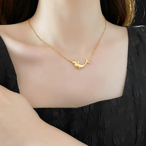 Macro detail of a golden whale pendant necklace with zircon on a model's collarbone