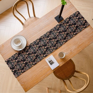 Floral print table runner with pink blossoms on black fabric over a wooden dining table