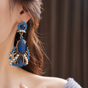 Close-up of vintage gold earrings with blue gemstones and pearls worn by a model