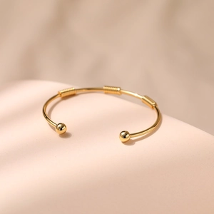 Macro detail of gold open bangle featuring spherical ends and spiral metal ornaments