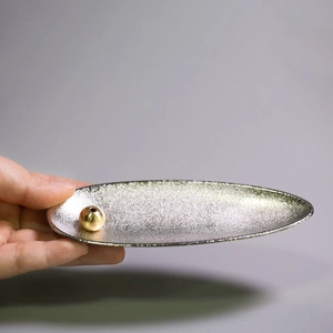Close-up of a silver matte finish incense tray with a gold spherical holder in hand