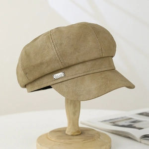 Detail of khaki faux suede newsboy hat featuring a rectangular metal fashion badge