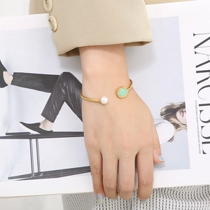 Gros plan d'un bracelet doré avec perle et pierre verte sur fond de magazine de mode