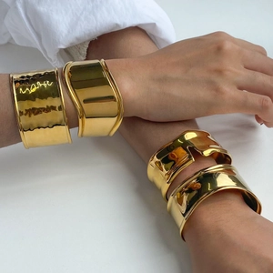 Detailed view of wide gold cuffs with hammered and smooth finishes on a model
