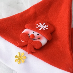 Close-up of plush snowman applique and gold glitter snowflake on a red Christmas hat