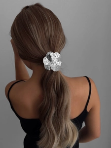 Detail of a silver flower-shaped metal hair tie on a model's low ponytail with hammered texture