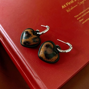 Close-up of heart-shaped leopard print earrings with silver hooks on a vintage red book