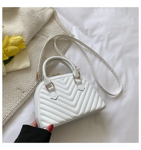 Detailed view of a white quilted shell bag on soft bedding with elegant floral accents