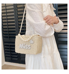 Detail of beige woven straw bag featuring pearl Miss lettering and a heart-shaped ornament