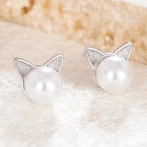 Close-up of pearl stud earrings with silver cat ear design on a textured surface