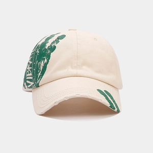 Close-up of cream cotton baseball cap with green hand graffiti and distressed brim details
