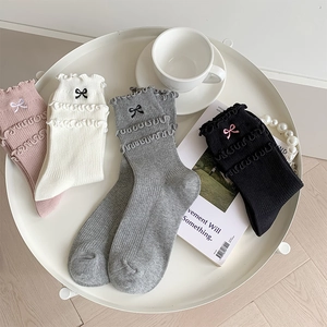 Detailed view of ruffle cuff socks with bow embroidery in four pastel colors on a tray