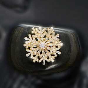 Rotating snowflake zircon brooch pin in gold finish on natural dark stone backdrop