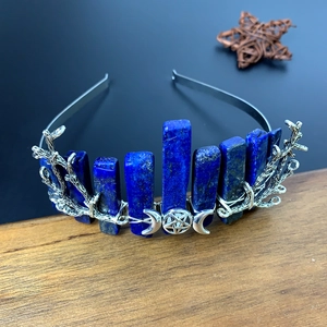 Detail of silver crescent moon crown with blue crystals and branch texture on wood