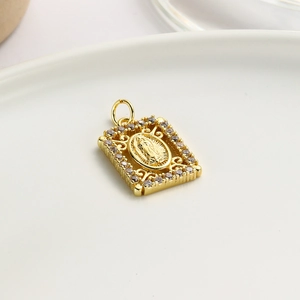 Detail of gold plated Virgin Mary pendant with cubic zirconia on white ceramic tray