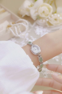 Elegant silver oval watch with green jade-like stones worn on wrist with floral background
