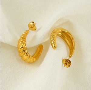 Detailed view of 18K gold plated twisted rope hoop earrings on soft beige fabric background