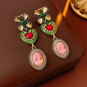 Détail de boucles d'oreilles cœur vintage avec émail vert et camée rose sur du cuir