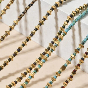 Detail of 18K gold stainless steel beads and colorful gemstone necklaces on white stone