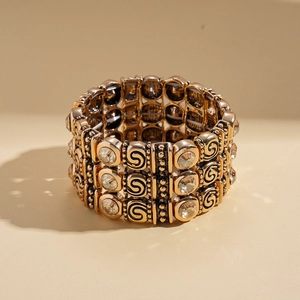 Detail of vintage gold-tone elastic bangle with swirl relief patterns and clear rhinestones