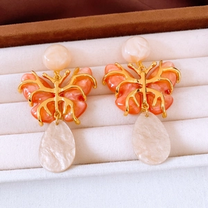 Macro detail of vintage resin butterfly earrings with golden metal and coral orange inlay