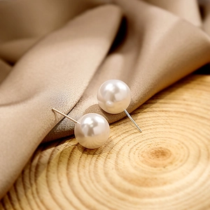 Elegant geometric pearl stud earrings on a rustic wood slice and brown silk fabric