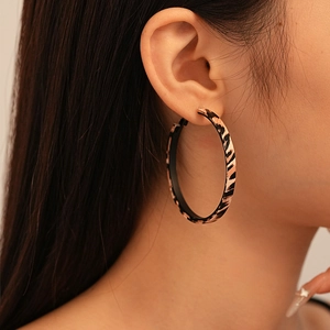 Close-up of a model wearing large leopard print hoop earrings with geometric pattern