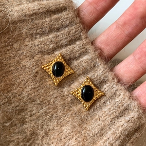 Boucles d'oreilles vintage dorées avec pierre noire ovale sur texture de pull marron