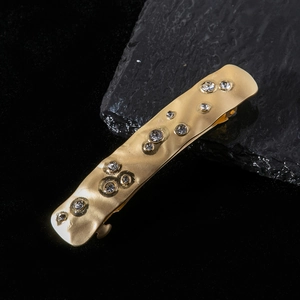 Macro shot of gold-plated metal hair clip with rhinestones and textured surface