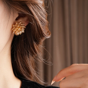 Close-up of elegant gold flower stud earrings with sparkling zircons worn by a model