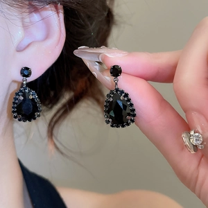 Detailed view of silver teardrop earrings featuring black gemstones and halo diamonds