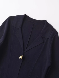 Detail of navy knit cardigan featuring a textured lapel and a gold flower-shaped button