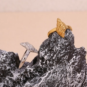 Detailed view of two vintage conch shell rings in gold and silver finish on a grey rock