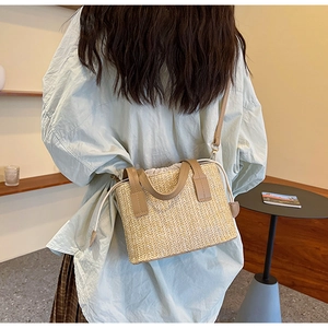 Woman wearing the woven straw tote bag with brown leather handles in a minimal interior