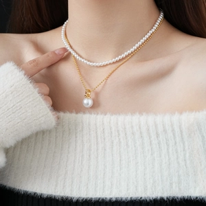 Close-up of layered gold plated necklace featuring elegant white pearls and round pendant