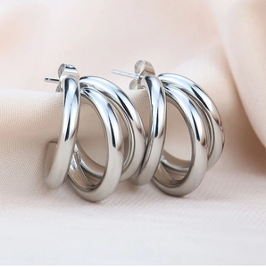 Macro shot of silver triple-layered C-shape stainless steel earrings on silk