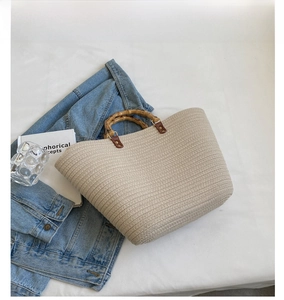 Detail of creamy white woven tote bag featuring natural bamboo handles on a white surface