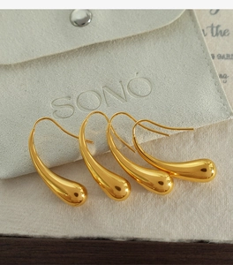 Detailed view of polished gold teardrop hook earrings displayed on a premium gray velvet pouch