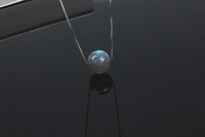 Macro shot of natural labradorite pendant with blue sheen on a sleek black mirror surface