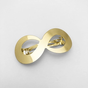 Macro shot of gold metallic infinity symbol hair clip showing glossy finish and spring mechanism