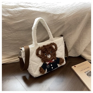 Detail of white quilted tote bag featuring a brown teddy bear and adjustable strap
