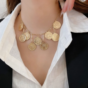 Detailed close-up of a gold multi-coin pendant necklace styled on a white shirt