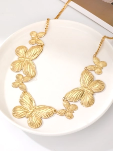 Detail of golden butterfly charm chain with textured wings on a white ceramic plate