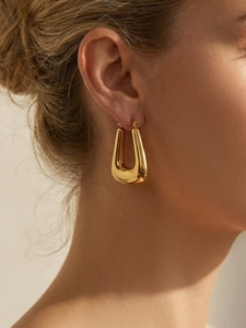 Close-up of chunky gold-plated U-shaped earrings on model showing mirror finish