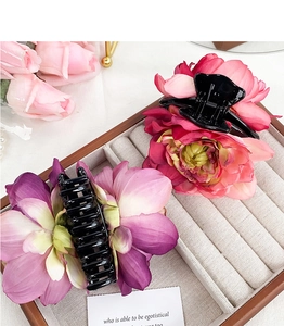 Detail view of two large floral hair claws in vibrant red and purple on a jewelry tray
