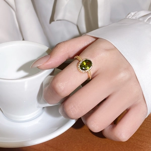 Detail of 18k gold plated ring with oval green gemstone and diamond halo on finger